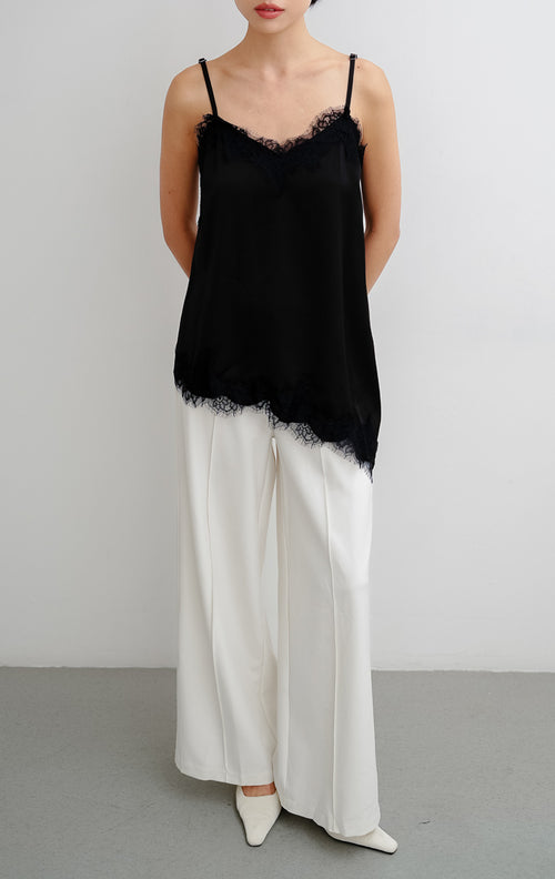 Atasan tank top wanita warna hitam (black) Zilia Top berbahan satin halus dengan renda (lace trim) dan potongan bawah asimetris (asymmetrical hem).