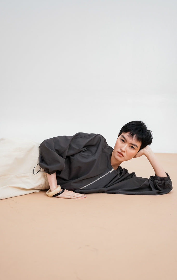 Model berpose mengenakan Zoria Jacket warna dark grey, jaket zip-up dengan siluet lengan balloon, kerah bulat, dan detail pergelangan tangan elastis