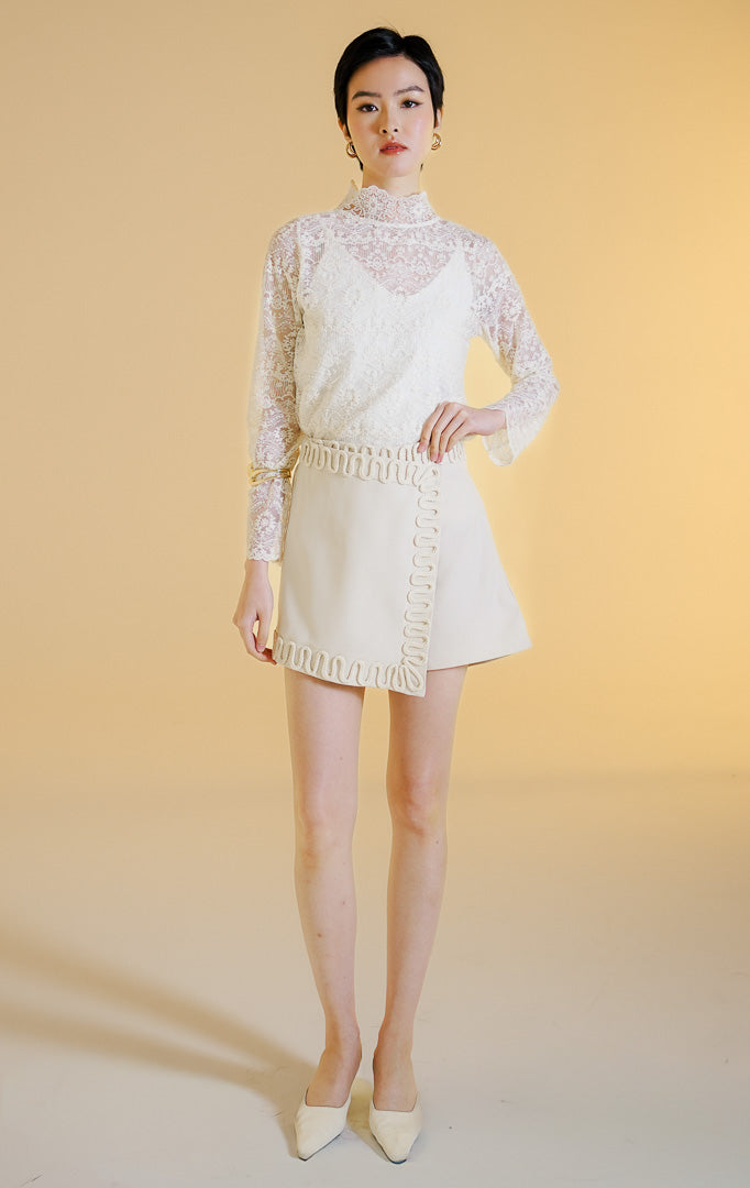 Pakaian wanita model celana rok mini gaya rapi (tailored skort) dengan detail lis hiasan tali di sepanjang tepi (rope trim) warna ivory Elvio Skort untuk gaya kasual chic yang elegan. 