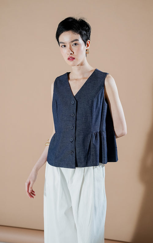 Agatha Vest Indigo dari This Is April, rompi tanpa lengan wanita warna biru indigo dengan kancing depan, leher V-neck, dan detail ruffle di bagian bawah.