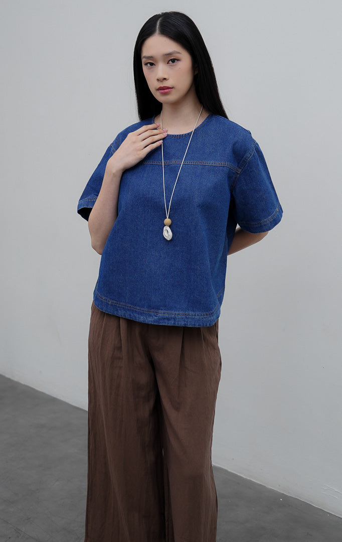 Atasan wanita lengan pendek berbahan denim warna biru (denim) Avenia Top dengan potongan boxy oversized, kerah bulat (round neckline), dan kancing belakang.