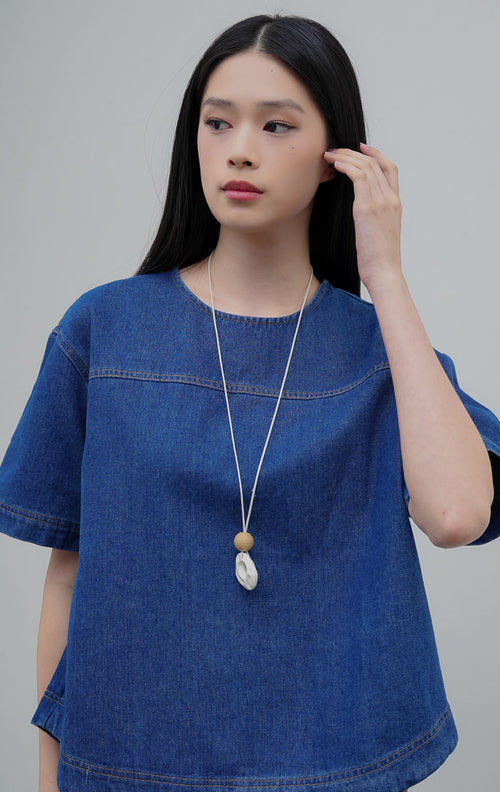 Atasan wanita lengan pendek berbahan denim warna biru (denim) Avenia Top dengan potongan boxy oversized, kerah bulat (round neckline), dan kancing belakang.