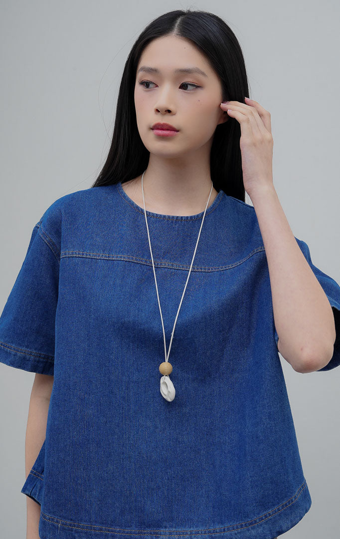 Atasan wanita lengan pendek berbahan denim warna biru (denim) Avenia Top dengan potongan boxy oversized, kerah bulat (round neckline), dan kancing belakang.