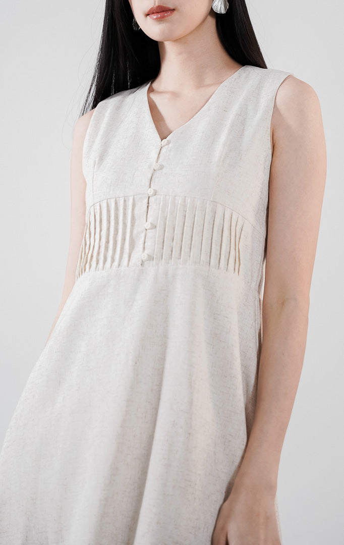 Aurynn Dress warna ivory, gaun midi A-line tanpa lengan berbahan katun dengan detail pintuck di dada, dipadukan dengan sandal hak putih.