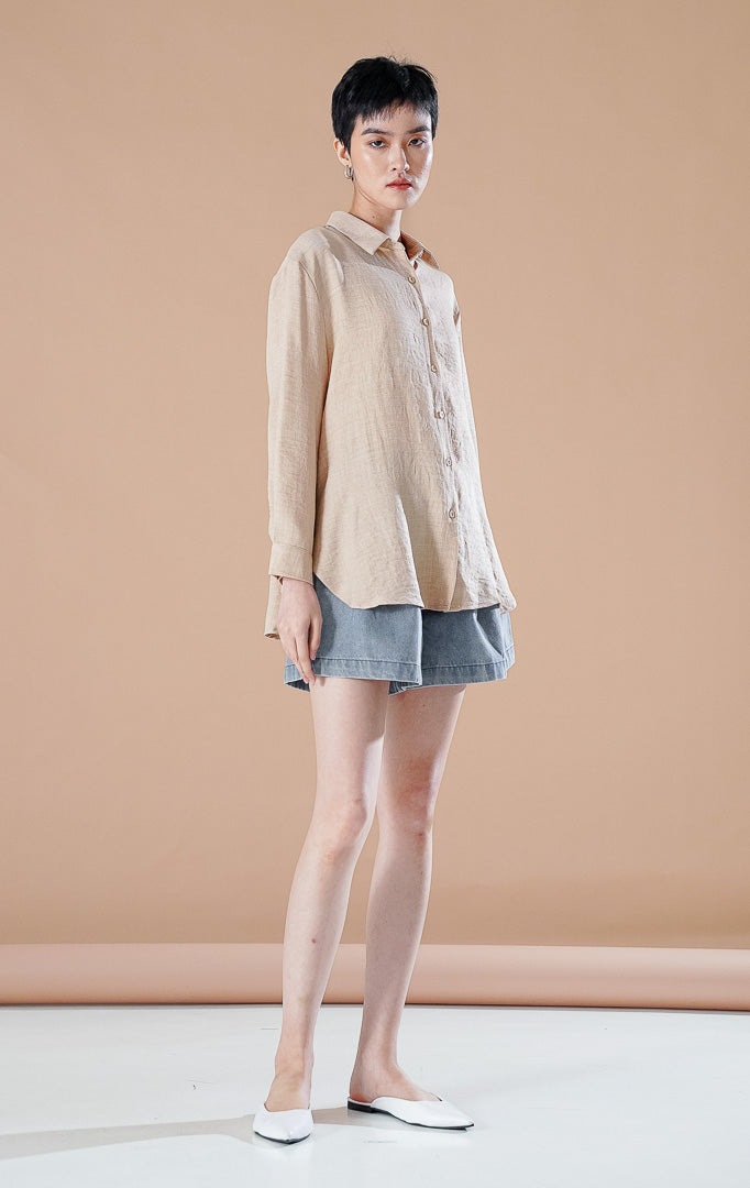 Kemeja basic lengan panjang berkerah Carolina Top berwarna khaki berbahan katun bertekstur, dipadukan dengan celana pendek denim dan sepatu flat putih