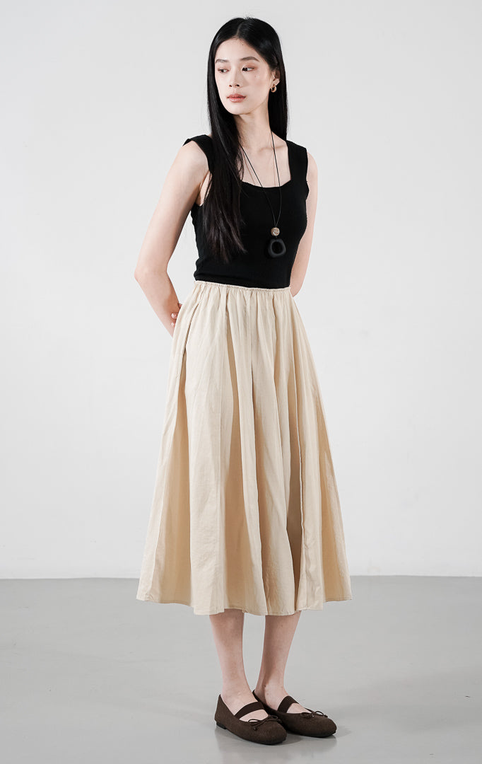  Catarina Skirt warna khaki (krem), rok midi potongan A-line dengan detail lipit (gathered) natural, dipadukan dengan atasan tanpa lengan warna hitam.