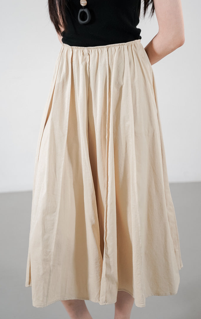  Catarina Skirt warna khaki (krem), rok midi potongan A-line dengan detail lipit (gathered) natural, dipadukan dengan atasan tanpa lengan warna hitam.