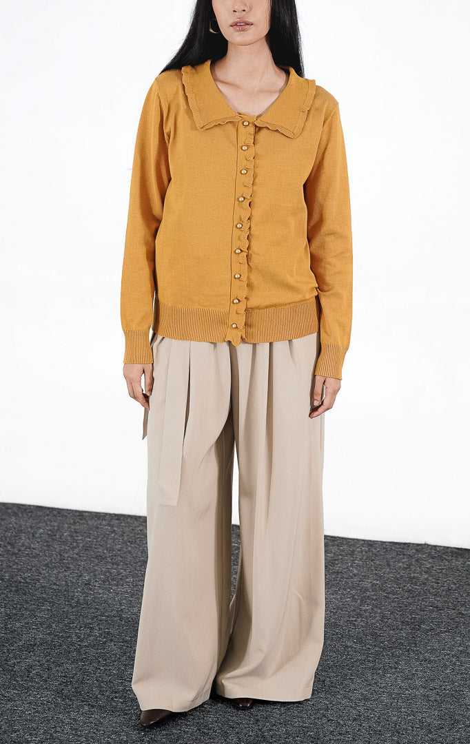  Catriona Top warna mustard, atasan rajut lengan panjang dengan detail kerah ruffle dan kancing emas bulat, dipadukan dengan celana kulot warna krem.