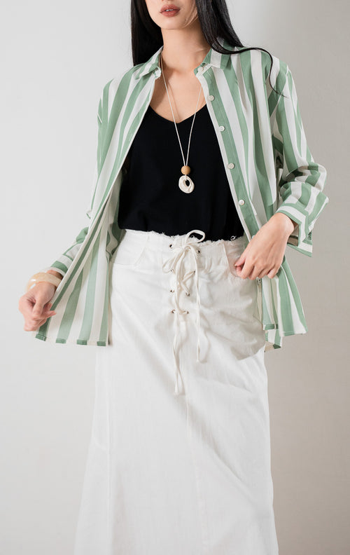 Kemeja lengan panjang motif garis vertikal hijau dan putih Kyoto Top berbahan ringan sebagai luaran atau outer, dipadukan dengan tank top hitam di bagian dalam dan rok panjang berwarna putih