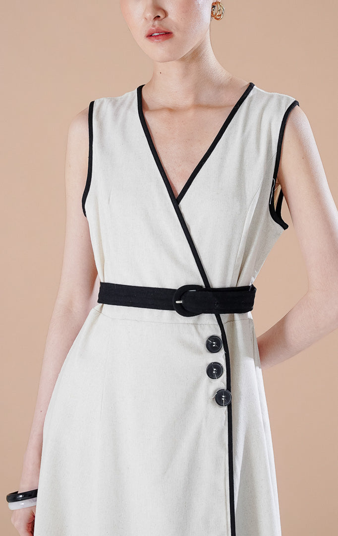Leana Dress Ivory berwarna putih tulang dengan detail garis hitam di sepanjang kerah V, kancing asimetris, dan sabuk hitam di pinggang.