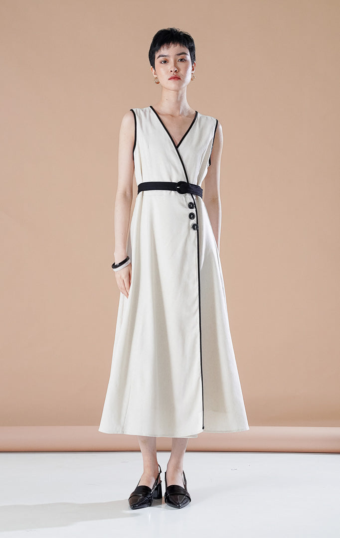 Leana Dress Ivory berwarna putih tulang dengan detail garis hitam di sepanjang kerah V, kancing asimetris, dan sabuk hitam di pinggang.