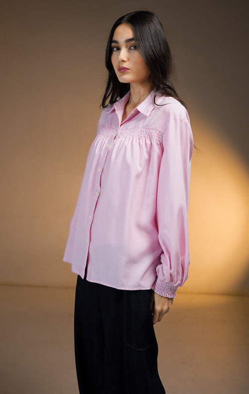 Model wanita mengenakan Osiana Smocked Long Sleeve Shirt warna pink, kemeja lengan panjang motif garis vertikal halus (pinstripe) dengan detail kerutan smock di bagian dada, dipadukan dengan celana denim gelap