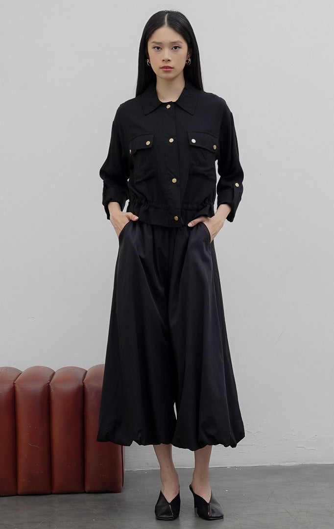 Kemeja utility wanita warna hitam (black) Piyora Top berbahan cotton linen dengan dua saku depan (dual pockets), tali pengikat lengan (roll-up sleeve straps), dan tali serut bagian bawah (drawstring hem).