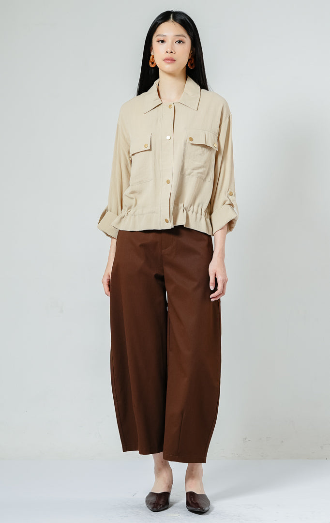 Kemeja utility wanita warna khaki Piyora Top berbahan cotton linen dengan dua saku depan (dual pockets), tali pengikat lengan (roll-up sleeve straps), dan tali serut bagian bawah (drawstring hem).