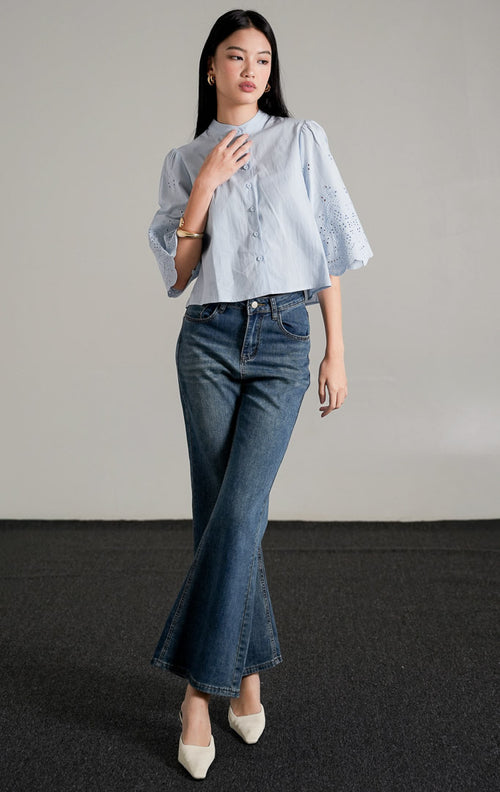  Rochelle Top Light Blue, kemeja katun biru muda dengan detail bordir eyelet pada lengan pendek yang melebar, dipadukan dengan celana jeans wide-leg.