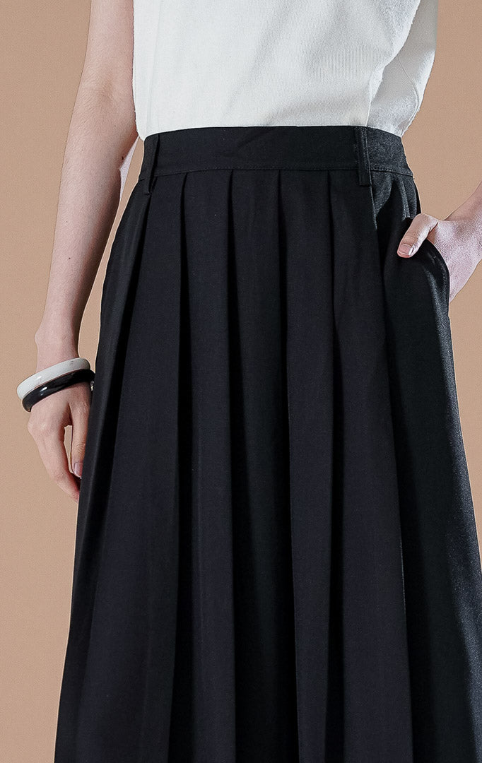 Sonali Skirt Black, rok panjang hitam dengan detail lipit (pleats) yang mengalir, saku depan fungsional, dan ban pinggang yang rapi.