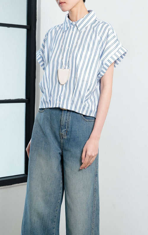 Kemeja crop wanita lengan pendek motif salur biru putih (blue white striped) Addie Top dengan kerah kemeja (pointed collar), bukaan kancing depan, saku depan (patch pocket), dan kelim melengkung (curved hem).