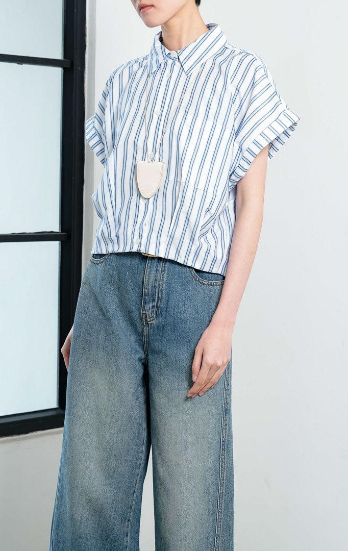 Kemeja crop wanita lengan pendek motif salur biru putih (blue white striped) Addie Top dengan kerah kemeja (pointed collar), bukaan kancing depan, saku depan (patch pocket), dan kelim melengkung (curved hem).