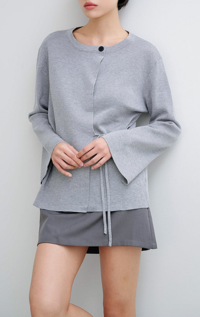 Cardigan rajut wanita warna abu-abu Addison Cardigan This Is April dengan siluet wrap, detail tali samping (side tie), kerah bulat, dan kancing dekoratif di bahu.