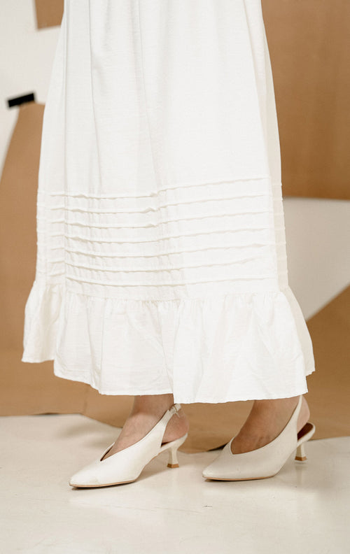 Model mengenakan Adonis Pintuck Ruffles Maxi Skirt White, produk rok panjang putih wanita dengan detail pintuck dan ruffles anggun, dipadukan dengan atasan cokelat. 