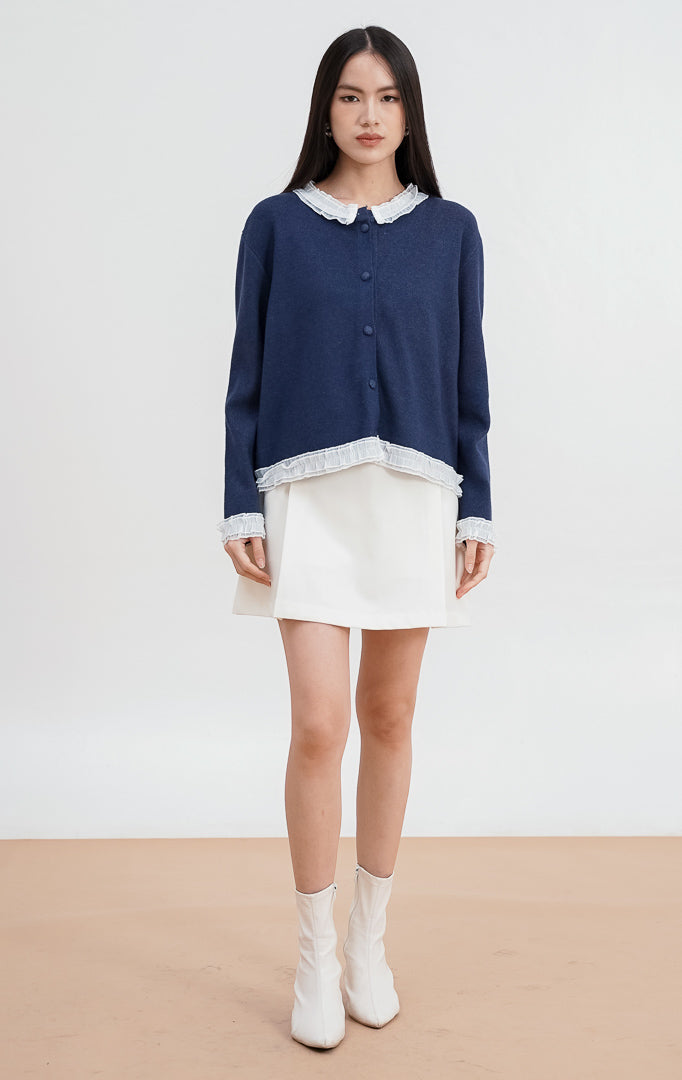 Close-up model mengenakan Aiko Cardigan warna navy, menampilkan detail kerah ruffle lace putih yang kontras dan kancing bungkus rajut di bagian depan.