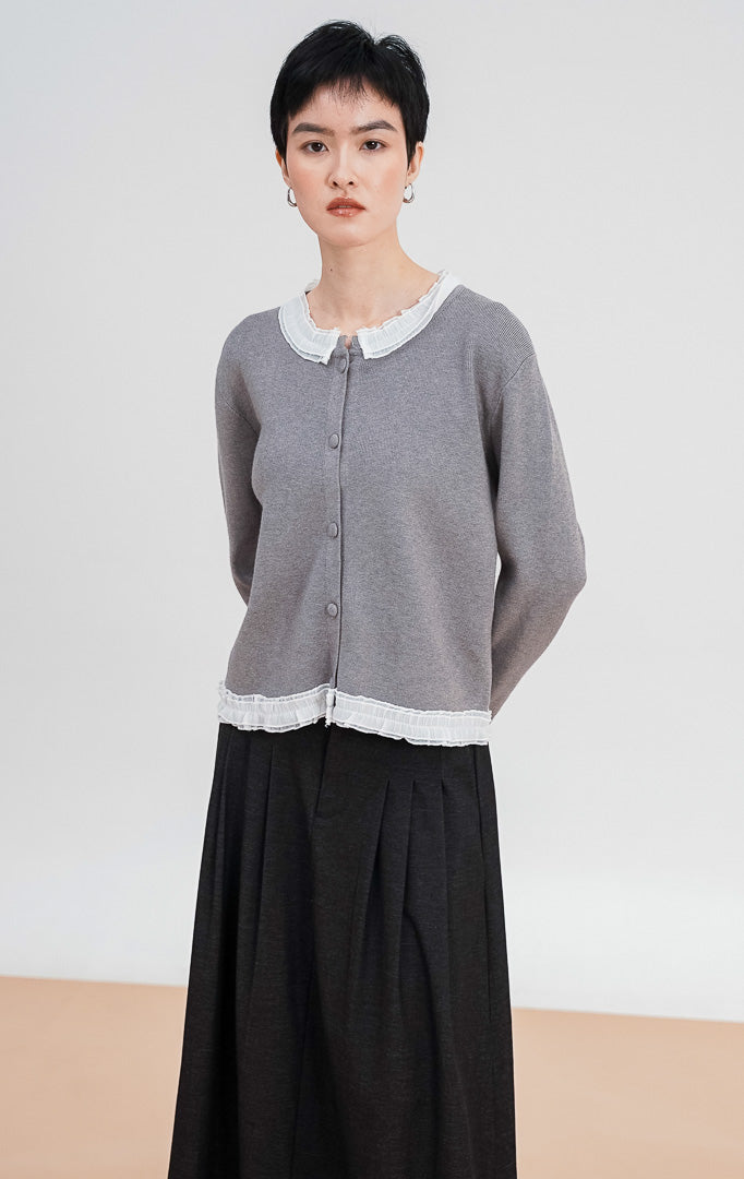 Model mengenakan Aiko Cardigan warna grey, menampilkan detail kerah ruffle lace putih yang cantik, material rajut halus, dan kancing bungkus di bagian depan.