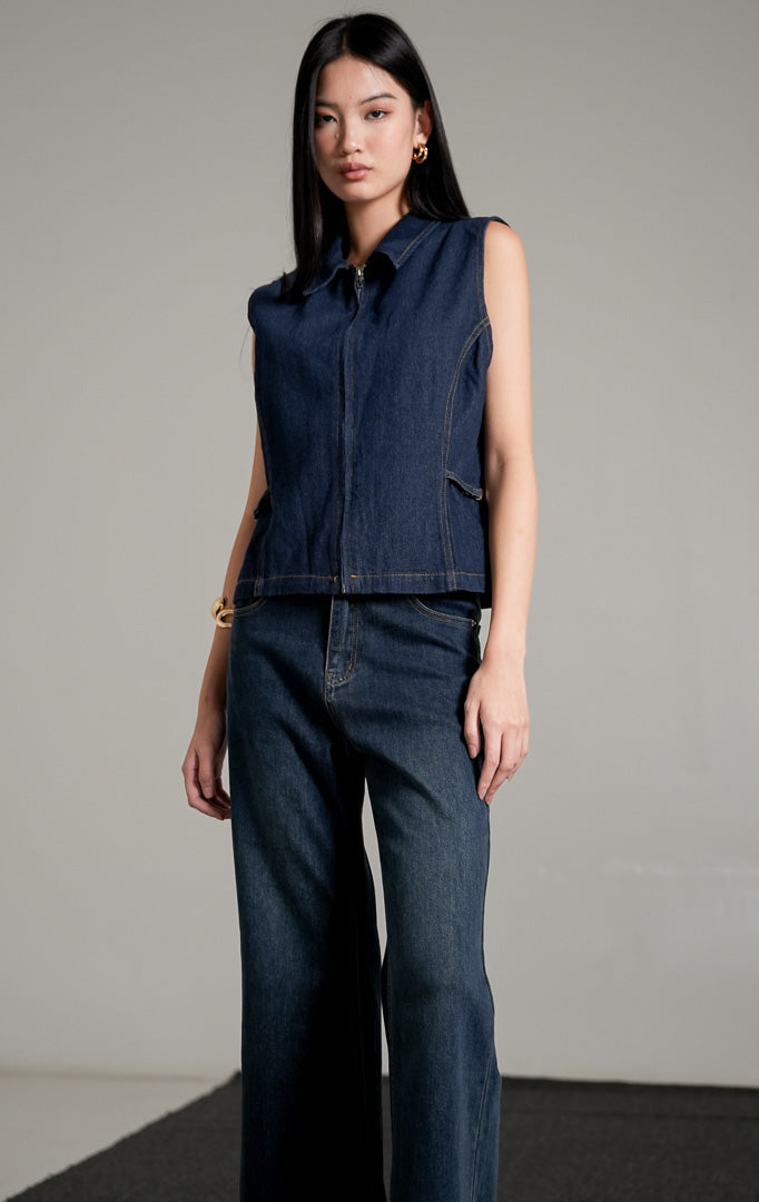 Alice Vest Indigo, sebuah rompi denim tanpa lengan berwarna biru dongker dengan kerah, dipadukan dengan celana jeans panjang senada.