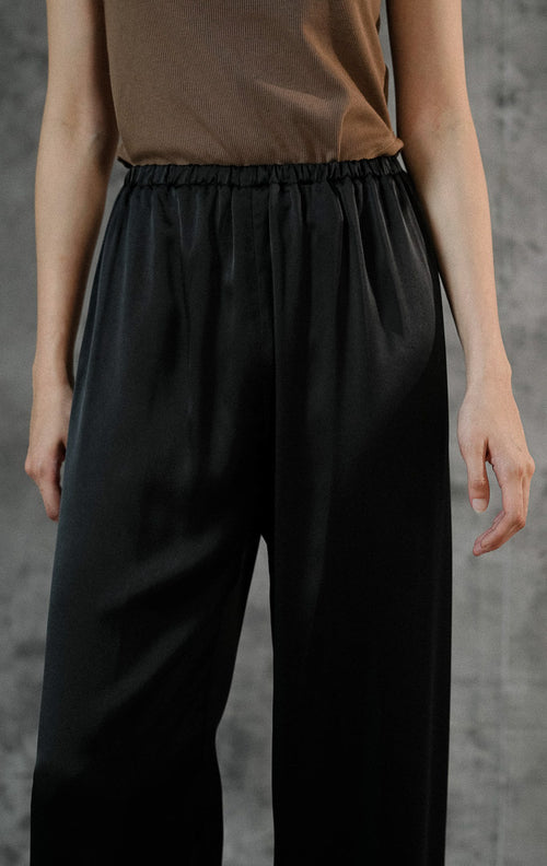 Celana panjang wanita Alonie Pants Black berbahan satin polos premium warna hitam dengan detail pinggang karet elastis untuk gaya casual chic. 