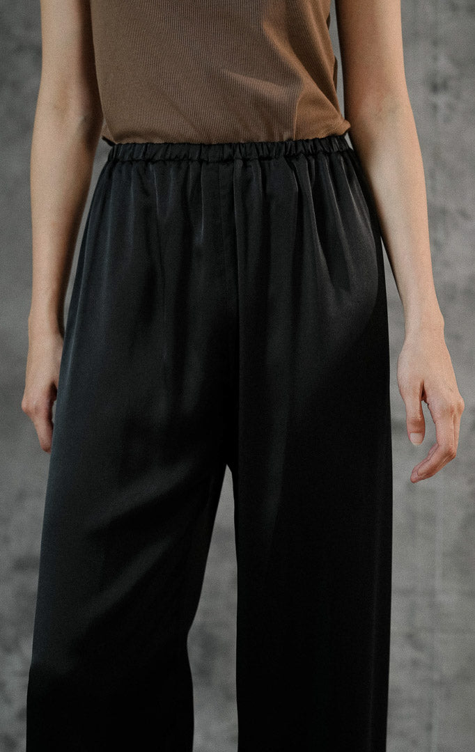Celana panjang wanita Alonie Pants Black berbahan satin polos premium warna hitam dengan detail pinggang karet elastis untuk gaya casual chic. 
