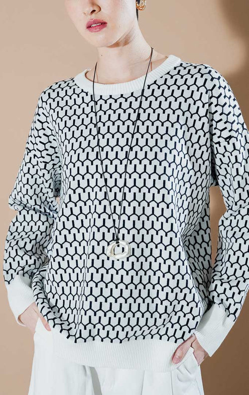 Model wanita mengenakan Amelie Sweater Black, atasan rajut putih dengan motif geometris hitam yang modern dan stylish dari This Is April.