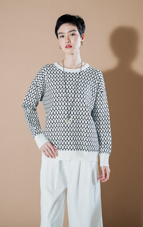 Model wanita mengenakan Amelie Sweater Black, atasan rajut putih dengan motif geometris hitam yang modern dan stylish dari This Is April.