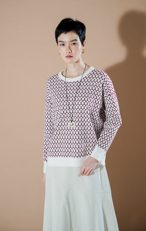 Model wanita mengenakan Amelie Sweater Red, atasan rajut motif geometris berwarna merah dan putih dengan kerah bulat (round neck) yang stylish dari This Is April.
