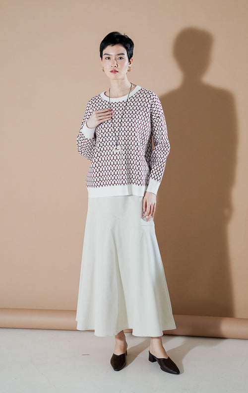 Model wanita mengenakan Amelie Sweater Red, atasan rajut motif geometris berwarna merah dan putih dengan kerah bulat (round neck) yang stylish dari This Is April.