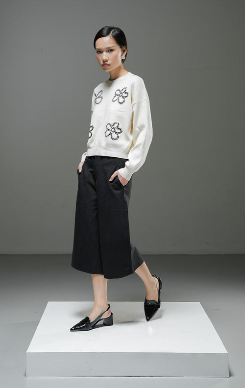 Sweater rajut wanita Amora Sweater warna ivory krem muda lengan panjang dengan motif bordir bunga besar warna hitam, kerah bulat, dan detail ribbed hem. 