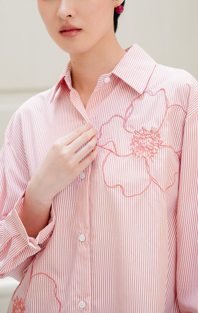 Kemeja lengan panjang wanita Amour Top warna pink peach bermotif stripe (salur) dengan detail bordir bunga (floral embroidery) dan kancing depan. 