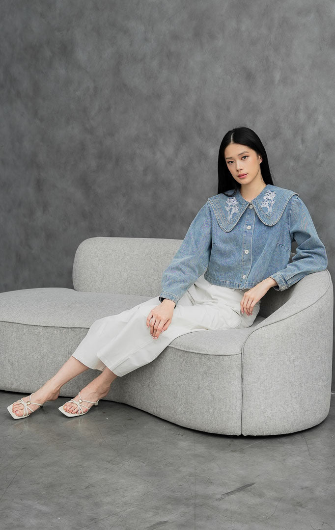 Atasan denim wanita lengan panjang warna biru muda (light denim) Anastasia Top berbahan non-stretch dengan kerah besar oversized Peter Pan collar berhias bordir bunga putih.