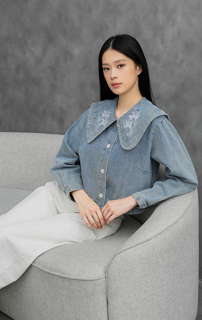 Atasan denim wanita lengan panjang warna biru muda (light denim) Anastasia Top berbahan non-stretch dengan kerah besar oversized Peter Pan collar berhias bordir bunga putih.