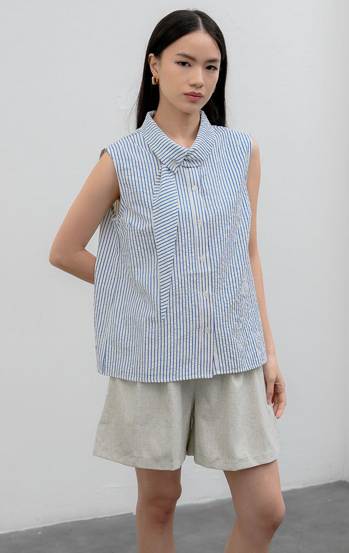 Atasan sleeveless blouse wanita warna biru (blue) Anestassia Top bermotif garis vertikal (striped) berbahan crinkle polyester dengan aksen kerah draped dan tali ikat (tie detail).