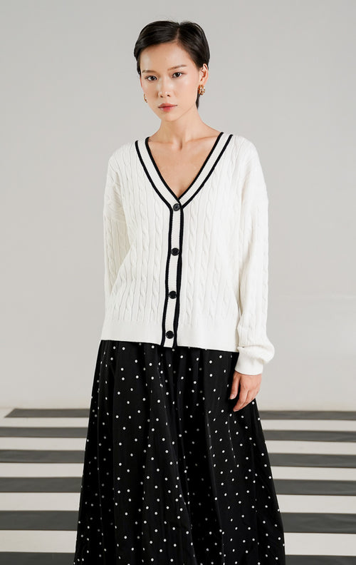 Kardigan rajut wanita Annette White dengan pola cable knit (kepang), kerah V neck bergaris hitam, dan kancing depan hitam dari This Is April. 