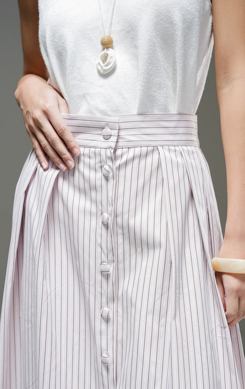Rok midi wanita Artemis Skirt warna light pink merah muda lembut motif salur garis vertikal dengan kancing depan berlaput kain, detail pleat, dan pinggang karet. 