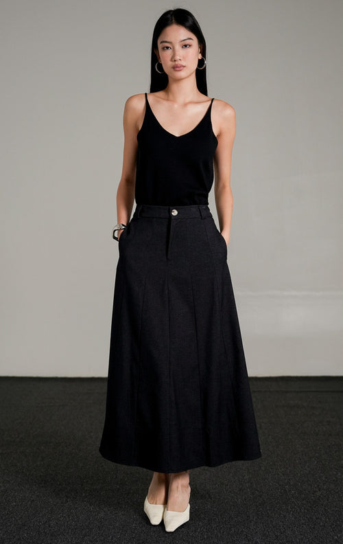 Ashton A-line Skirt berwarna dark denim dengan kancing depan, dipadukan dengan atasan tank top hitam dan sepatu heels putih.