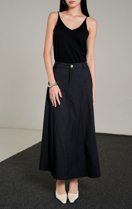 Ashton A-line Skirt berwarna dark denim dengan kancing depan, dipadukan dengan atasan tank top hitam dan sepatu heels putih.