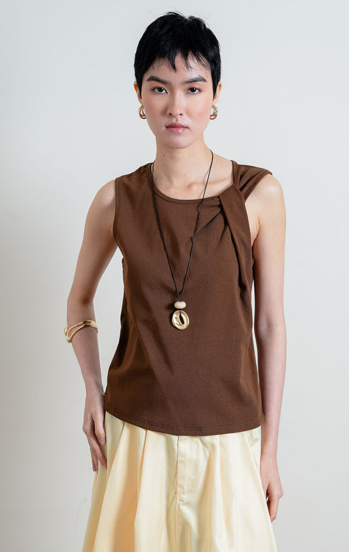 Atasan wanita tanpa lengan warna cokelat (brown sleeveless top) Aspen Top berbahan kain jersey lembut dan halus (soft, smooth jersey fabric) dengan kerah bulat (rounded neckline) dan detail aksen simpul kain di bagian depan (statement tie detail). 