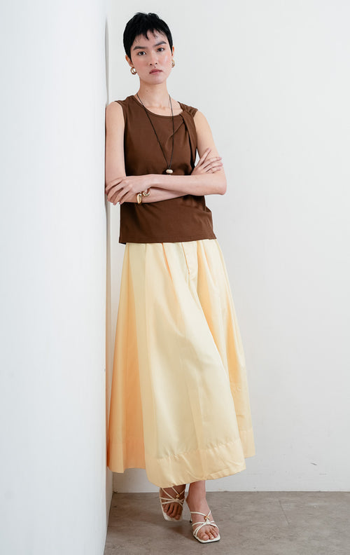Atasan wanita tanpa lengan warna cokelat (brown sleeveless top) Aspen Top berbahan kain jersey lembut dan halus (soft, smooth jersey fabric) dengan kerah bulat (rounded neckline) dan detail aksen simpul kain di bagian depan (statement tie detail). 