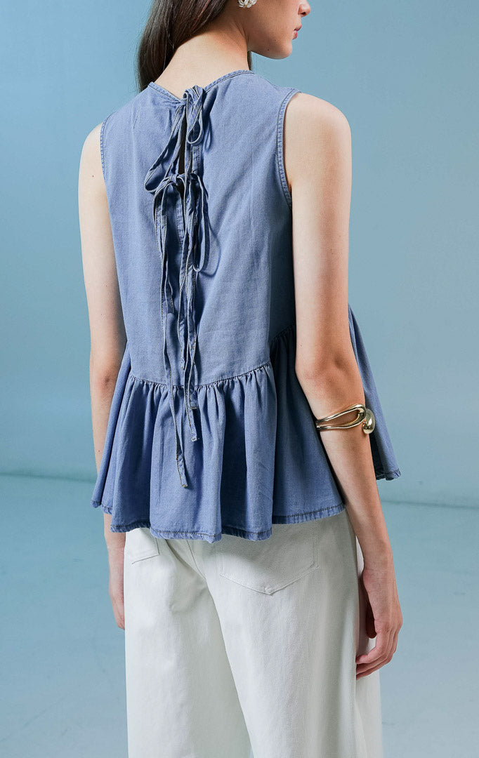 Model wanita mengenakan Elvera Sleeveless Peplum Top warna biru denim, atasan tanpa lengan wanita berbahan denim dengan siluet peplum (mengembang di bawah) yang feminin. 