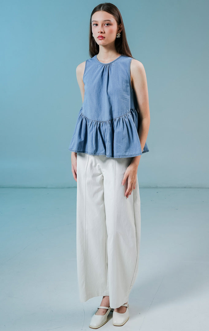 Model wanita mengenakan Elvera Sleeveless Peplum Top warna biru denim, atasan tanpa lengan wanita berbahan denim dengan siluet peplum (mengembang di bawah) yang feminin. 
