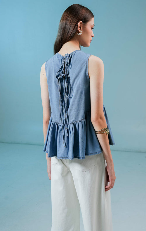 Model wanita mengenakan Elvera Sleeveless Peplum Top warna biru denim, atasan tanpa lengan wanita berbahan denim dengan siluet peplum (mengembang di bawah) yang feminin. 
