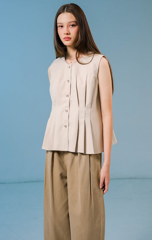 Model wanita mengenakan Cornelia Pleats Sleeveless Top warna khaki, atasan tanpa lengan berbahan katun dengan detail lipit (pleats) yang elegan dan kancing depan. 