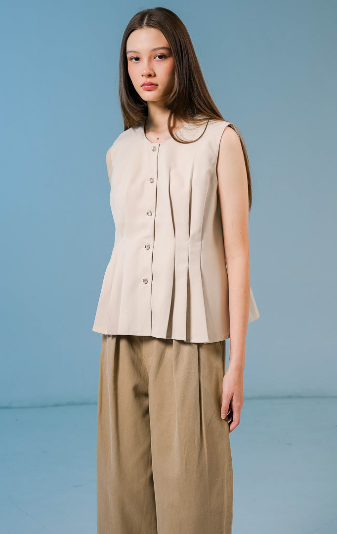 Model wanita mengenakan Cornelia Pleats Sleeveless Top warna khaki, atasan tanpa lengan berbahan katun dengan detail lipit (pleats) yang elegan dan kancing depan. 