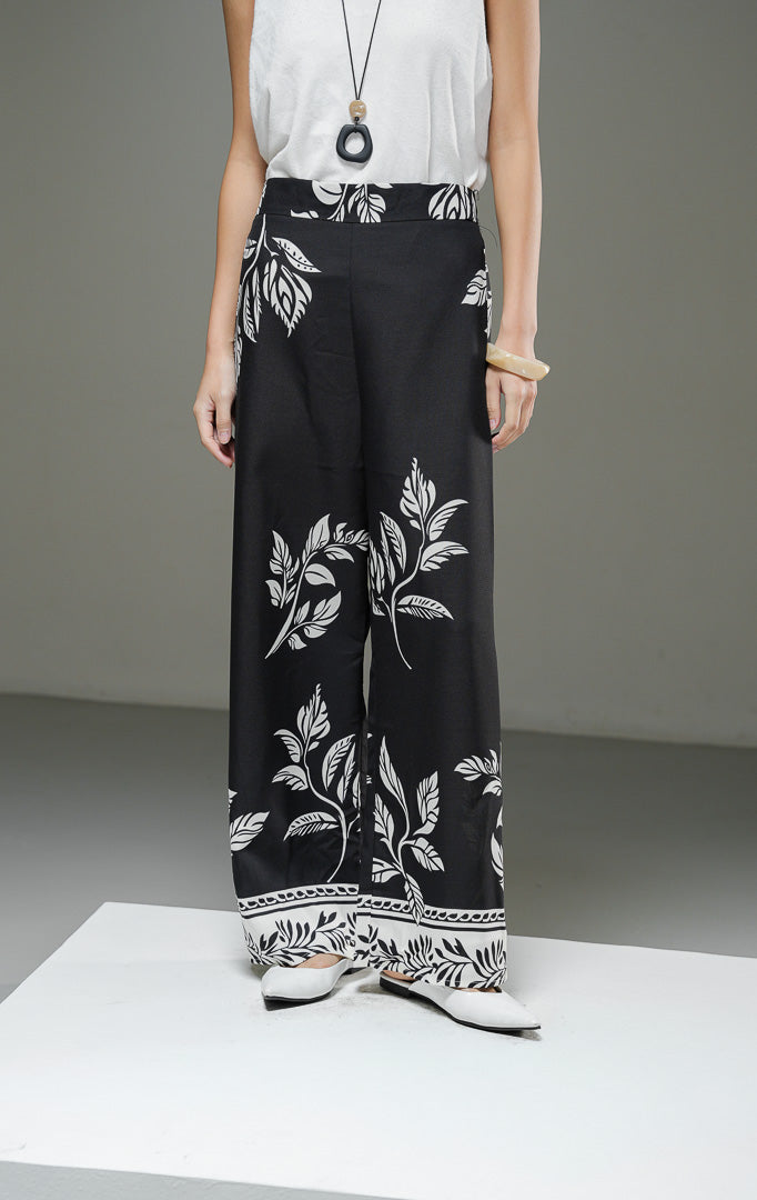Celana panjang wanita Beatrice Pants warna hitam dengan motif botanical daun dan bunga putih, potongan high waist straight leg, dan ban pinggang rapi.